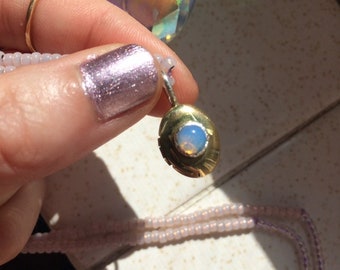 May include: A delicate gold pendant with a round opal stone set in a silver bezel. The pendant is hanging from a thin chain.