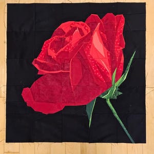 Puede incluir: Una rosa roja vibrante, representada de forma geométrica, destaca sobre un fondo cuadrado negro. Los pétalos de la rosa muestran diferentes tonos de rojo, con hojas y tallo verdes. La obra de arte es un contraste llamativo de color y forma.