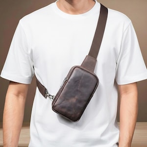 Puede incluir: Un bolso bandolera de cuero marrón con un compartimento principal con cremallera y una correa ajustable. El bolso se lleva cruzado, con la correa sobre el hombro. El bolso es de cuero envejecido.