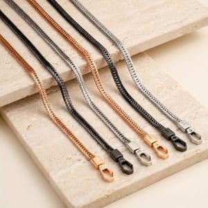 May include: Five flat herringbone chains in varying metallic finishes including rose gold, black, silver, and gunmetal. Each chain features a matching metal lobster claw clasp at the end, designed for secure attachment to bags or other accessories.