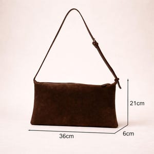 May include: A brown suede shoulder bag with a long, adjustable strap. The rectangular bag measures 14 inches long, 8 inches wide, and 2 inches deep. The bag has a simple design and is suitable for everyday use.