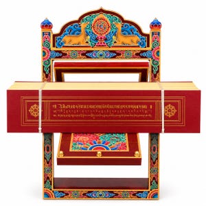 Peut inclure: Un support de livre en bois rouge orné de motifs floraux et animaliers colorés, incluant deux cerfs dorés entourant une roue centrale. Une boîte rectangulaire rouge avec des inscriptions tibétaines dorées est maintenue par des élastiques blancs.