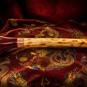 May include: A cane handle featuring a dark, polished, deep red bulbous grip connected by a metallic copper-colored band to a long, cylindrical, light-colored shaft with natural dark brown mottled markings along its length.
