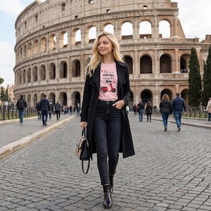 Könnte beinhalten: Eine Person trägt ein rosa T-Shirt mit einem roten Roller-Motiv und dem Text "Life is a Journey, Enjoy the Ride". Sie trägt einen schwarzen Trenchcoat, eine schwarze Jeans und schwarze Stiefel. Im Hintergrund ist das Kolosseum in Rom zu sehen.