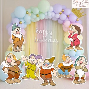Puede incluir: Un arco de globos en tonos pastel azul, verde, morado y amarillo con una corona dorada y un letrero blanco que dice happy birthday. Siete figuras recortadas de enanos de dibujos animados con trajes coloridos frente a los globos.