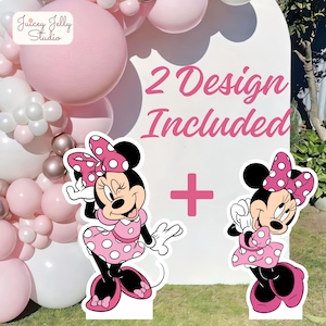Puede incluir: Dos recortes de Minnie Mouse con lunares rosas y blancos, con un lazo a juego. La imagen incluye el texto "2 Design Included" y un signo más rosa. Un arco de globos rosas y blancos está en el fondo.