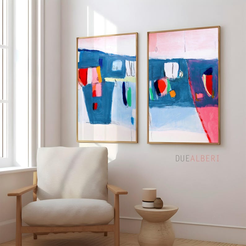 May include: Two framed abstract paintings with gold frames. The artwork features bold brushstrokes in blue, pink, red, and yellow. The paintings hang above a wooden chair and a small side table. The text "DUEALBERTI" is visible on the right painting.