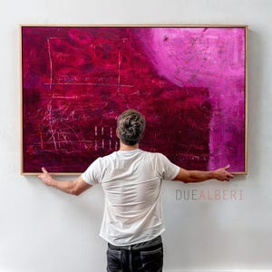 May include: A large rectangular abstract painting featuring deep magenta and vibrant pink tones with layered textures and thin white linear markings, enclosed in a light wood frame. The text DUEALBERI is printed in the lower right corner.