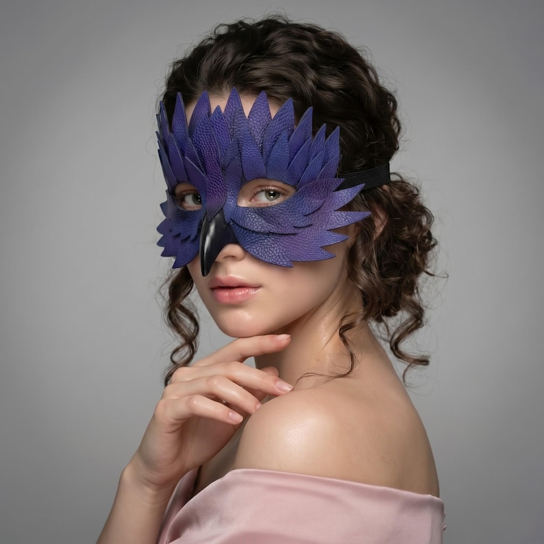 May include: A purple leather mask with a bird-like design, featuring layered feather details and a black beak. The mask is secured with a black elastic band. The mask is a costume accessory.