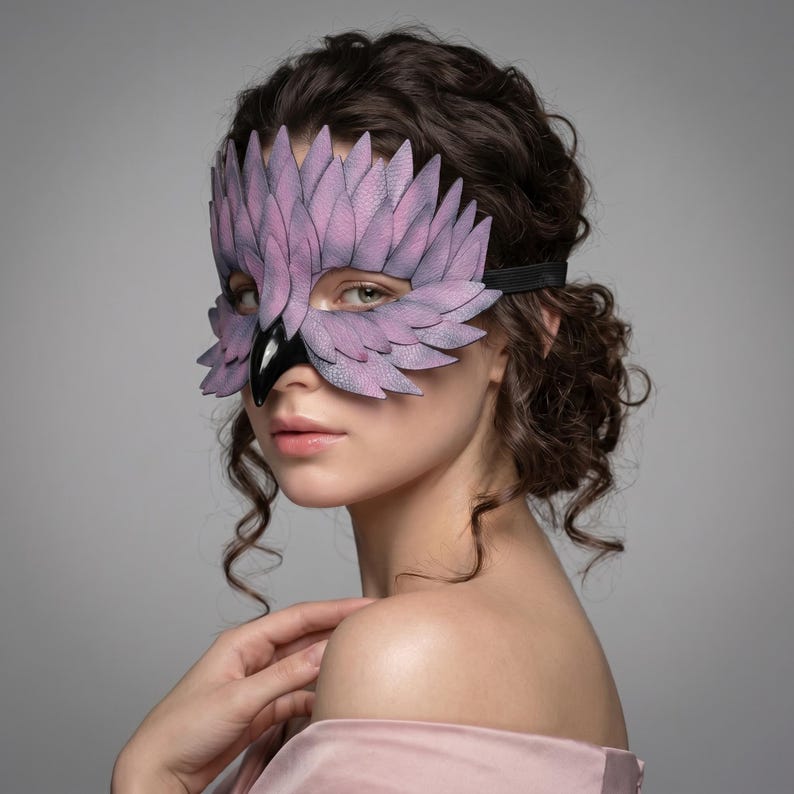 May include: A lavender and black bird-shaped mask with feather detailing. The mask has a black elastic band and a glossy black beak. The mask is worn over the eyes and nose. The mask is made of leather.