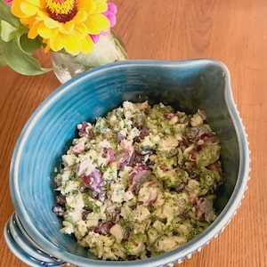 Könnte beinhalten: Eine blaue Schüssel gefüllt mit einem Brokkoli-Salat mit roten Trauben und Rosinen. Der Salat ist mit einem cremigen Dressing bedeckt.