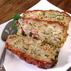 May include: A close-up of a sliced meatloaf with a red sauce on top. The meatloaf is made with minced meat, spinach, and other vegetables.