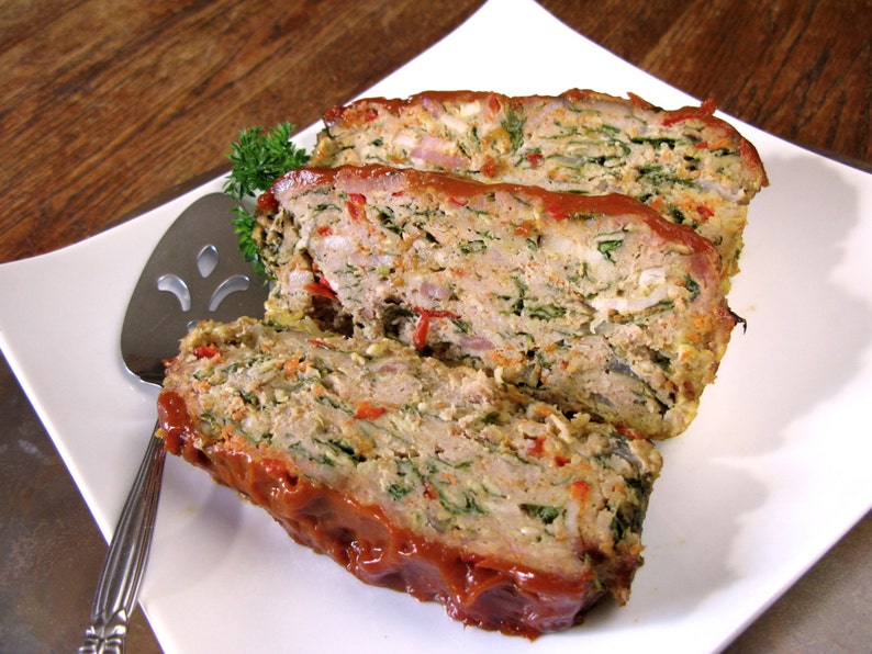 May include: A close-up of a sliced meatloaf with a red sauce on top. The meatloaf is made with minced meat, spinach, and other vegetables.