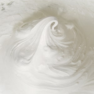 May include: Close-up of a white meringue mixture in a bowl, showing a swirling pattern created by beating the egg whites.