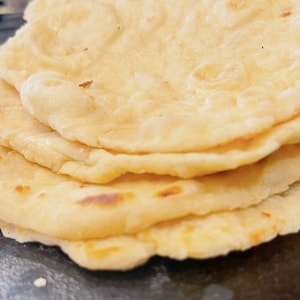 Könnte beinhalten: Ein Stapel von vier goldbraunen Fladenbroten, wahrscheinlich Tortillas, auf einer dunklen Oberfläche.