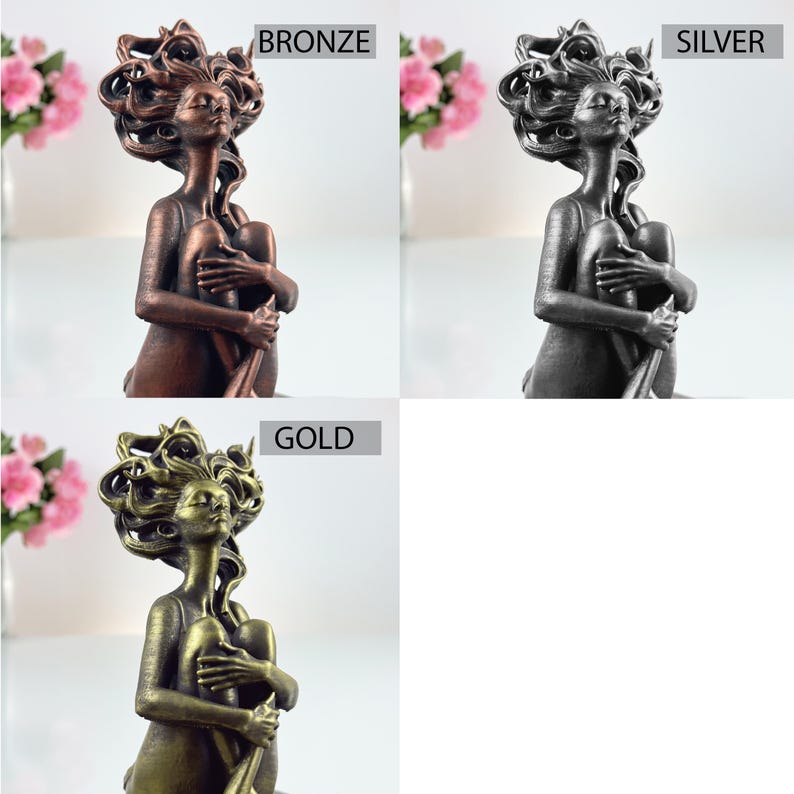 K&ouml;nnte beinhalten: Ein Set aus drei Statuen, die eine Figur mit flie&szlig;endem Haar darstellen, die mit an die Brust gezogenen Knien sitzt. Die Statuen sind mit BRONZE, SILVER und GOLD beschriftet und zeigen die Figur in drei verschiedenen Metalloberfl&auml;chen.
