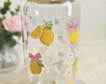 May include: A clear glass tumbler with a bamboo lid featuring a repeating pattern of yellow lemons, white daisies, and small pink gingham bows. The design is printed directly onto the exterior of the cylindrical glass container.