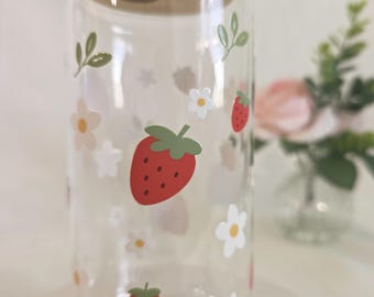 May include: A clear glass tumbler with a cylindrical shape, featuring a light-colored bamboo lid. The exterior of the glass is decorated with a repeating pattern of red strawberries, small white flowers with yellow centers, and green leaves.