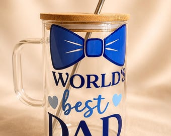 May include: A clear glass mug with a handle, a bamboo lid, and a metal straw. The front features a blue bow tie graphic above the text "WORLD'S best DAD" in blue lettering, accented by two small hearts in light blue and grey on either side of the word best.