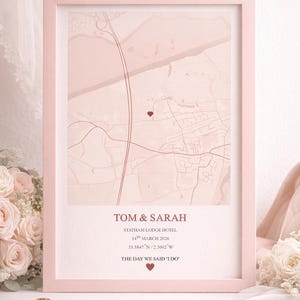 May include: A framed, blush-pink map print featuring the names "TOM & SARAH" and the text "THE DAY WE SAID 'I DO'". The map includes a heart-shaped marker and coordinates. The frame is a soft pink, and the overall theme is romantic.