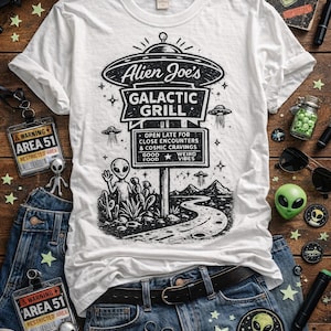 May include: White t-shirt featuring a black and white graphic of an alien diner, "Alien Joe's Galactic Grill." The shirt is styled with blue jeans, patches, and Area 51 themed accessories. The text on the shirt reads "Open Late for Close Encounters & Cosmic Cravings."