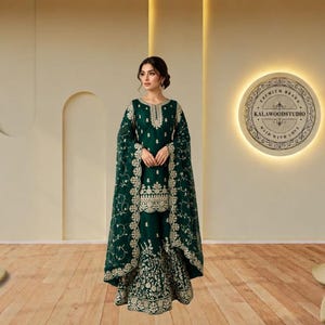 Könnte beinhalten: Ein dreiteiliges Ensemble in dunklem Smaragdgrün, bestehend aus einer knielangen Tunika, einer weiten Hose und einem passenden Dupatta. Das Kleidungsstück ist mit aufwendigen silbernen Stickereien am Ausschnitt, Saum und an den Rändern verziert.