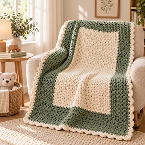 May include: A handmade crochet blanket featuring a central cream-colored rectangular panel surrounded by a wide sage green border. The entire blanket is finished with a decorative scalloped cream-colored edge, showcasing a textured yarn stitch pattern.