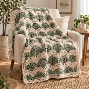 May include: A crochet blanket featuring a repeating scalloped shell pattern in alternating rows of sage green and cream yarn. The rectangular textile displays a textured, open-work design with a consistent stitch pattern throughout the entire piece.