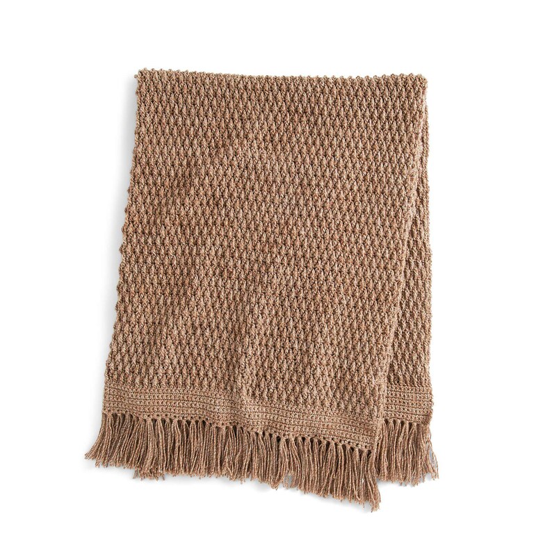May include: A tan-colored, textured throw blanket with a diamond pattern. The blanket has a fringed edge along the bottom. The blanket is made of a soft, woven material. The blanket is folded in half.