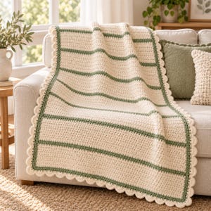 May include: A rectangular crochet blanket featuring wide cream-colored sections separated by thin horizontal sage green stripes. The blanket is finished with a decorative scalloped edge border in a matching sage green yarn throughout the perimeter.
