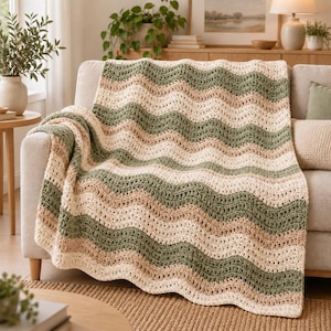 Può includere: Una coperta all'uncinetto con un motivo ripetitivo a onde o chevron. Il design è composto da strisce orizzontali ondulate in colori alternati verde salvia, beige tenue e crema, realizzate con un punto di lana testurizzato su tutto il pezzo.