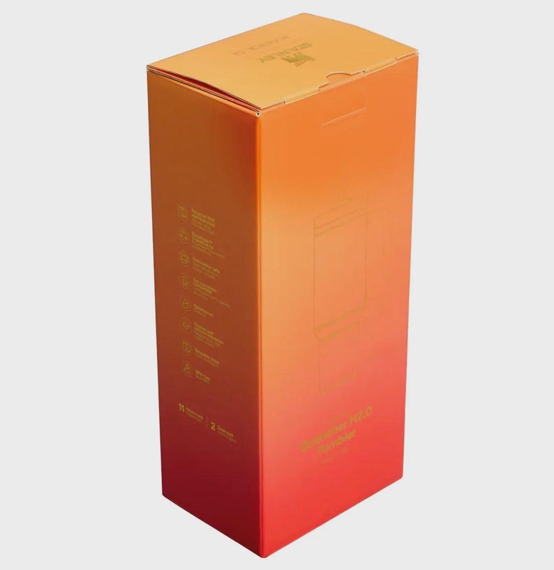 May include: A rectangular cardboard product box featuring a vertical gradient color scheme transitioning from orange at the top to red at the bottom. The box displays the Stanley brand logo, text reading Quencher H2.0 FlowState Tumbler, and icons.
