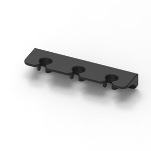 May include: A matte black, rectangular wall-mounted organizer featuring three circular cutouts along the front edge. The component has a flat top surface and a curved side profile, designed to hold three items securely in place within the slots.