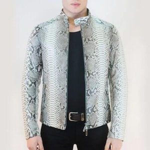 May include: A snakeskin-patterned jacket with a stand-up collar and a full-length zipper. The jacket is primarily gray and white, with a black shirt visible underneath. The model is wearing black pants and a black belt with a silver buckle.