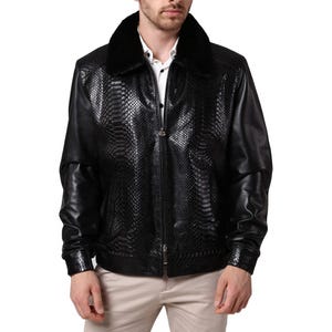 Könnte beinhalten: Eine schwarze Jacke mit strukturiertem Schlangenledermuster auf den Vorderteilen und glatten Lederärmeln. Das Kleidungsstück verfügt über einen schwarzen Kunstfellkragen, einen durchgehenden Frontreißverschluss und passende Ärmelbündchen.