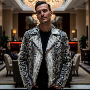 Puede incluir: Chaqueta de cuero con estampado de piel de serpiente en blanco y negro, con cierre de cremallera. La chaqueta tiene un estilo motero clásico con cuello de solapa y múltiples cremalleras. Se lleva sobre una camiseta negra.