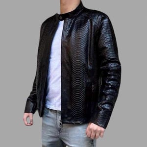 May include: Black faux leather jacket with a snakeskin texture. The jacket has a stand-up collar, a zipper closure, and a textured pattern. The jacket is worn over a white t-shirt and paired with gray jeans.