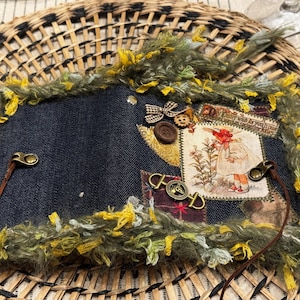 Puede incluir: Un parche de mezclilla hecho a mano con un borde decorativo de hilo verde y amarillo. Los adornos incluyen un pequeño lazo, botones y una imagen de estilo vintage de una niña. Las correas de cuero y los herrajes metálicos completan el diseño.