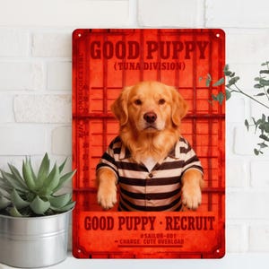 May include: A red metal sign featuring a golden retriever wearing a black and white striped shirt. The sign reads "GOOD PUPPY" and "GOOD PUPPY RECRUIT" with the text "CHARGE: CUTE OVERLOAD".