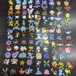 Puede incluir: Una colección de figuras de personajes coloridas, troqueladas, con varios diseños de criaturas animadas populares. Las figuras tienen varias formas y tamaños, con colores vibrantes y detalles. Las figuras están dispuestas sobre una superficie oscura.