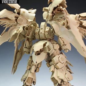 May include: A beige 1/100 scale statue of a detailed robot with large wing-like structures. The robot has intricate mechanical details and the text "NZ666-KSHATRIYA SPEC II" is visible at the top. The statue is on a gray surface.