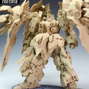 May include: A tan-colored 1/100 scale statue of a detailed robot, the NZ666-Kshatriya. The robot has large wing-like structures and intricate mechanical details. The statue is standing on a gray base. The text "NZ666-KSHATRIYA" and "1/100 STATUE" are visible.