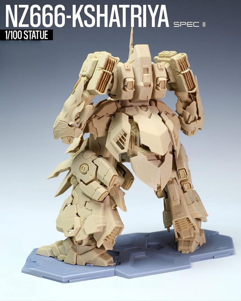 May include: A tan-colored, detailed statue of a robot, labeled "NZ666-KSHATRIYA SPEC II" and "1/100 STATUE". The robot is posed with its legs spread and arms bent, showcasing intricate mechanical designs and panels. It stands on a gray base.
