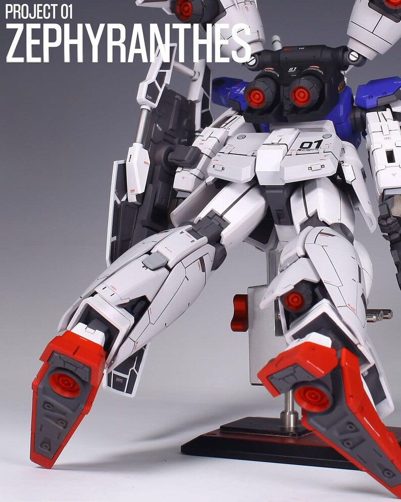 May include: A detailed model of a white and black robot with red and blue accents. The robot has intricate mechanical details, including visible joints, vents, and panels. The text "PROJECT 01 ZEPHYRANTHES" is visible in the upper left corner.