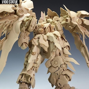 May include: A tan-colored Kshatriya model kit statue, with intricate mechanical details and large wing-like structures. The text "NZ666-KSHATRIYA SPEC II" and "1/100 STATUE" are visible. The statue is posed on a gray base.