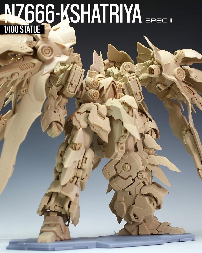 May include: A tan-colored Kshatriya model kit statue, with intricate mechanical details and large wing-like structures. The text "NZ666-KSHATRIYA SPEC II" and "1/100 STATUE" are visible. The statue is posed on a gray base.