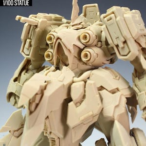 May include: A tan-colored 1/100 scale statue of the NZ666-Kshatriya Spec II, a detailed model with intricate mechanical designs. The statue features multiple panels, circular details, and a prominent head crest. The text "NZ666-KSHATRIYA" and "SPEC II" are visible.
