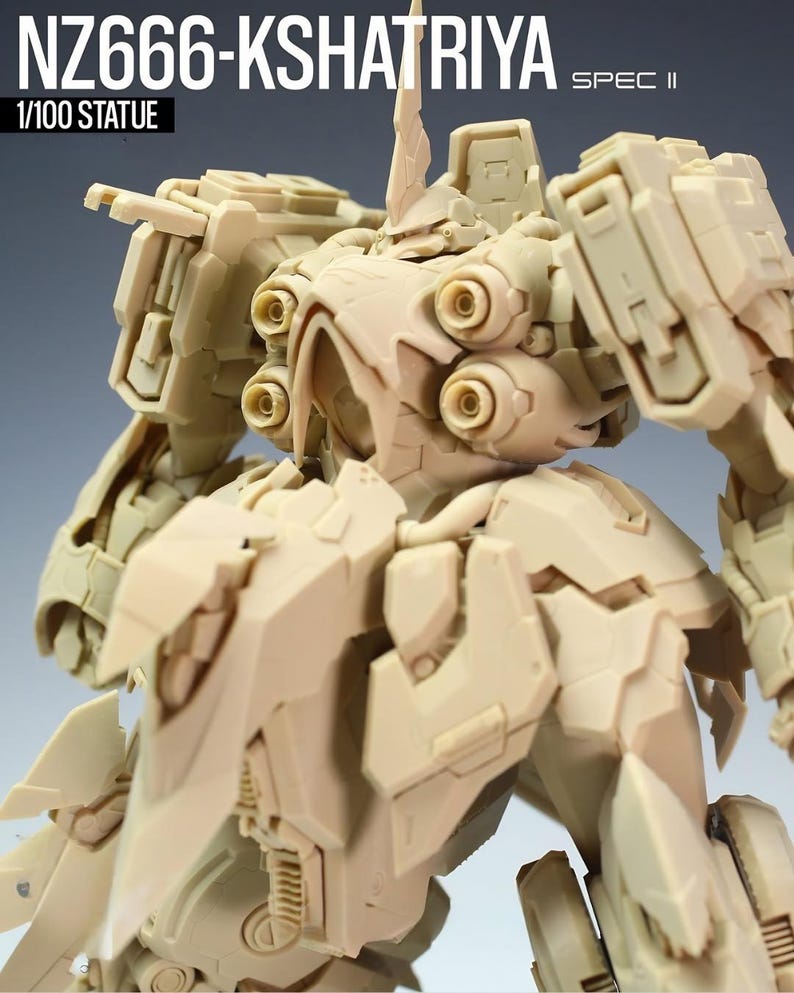 May include: A tan-colored 1/100 scale statue of the NZ666-Kshatriya Spec II, a detailed model with intricate mechanical designs. The statue features multiple panels, circular details, and a prominent head crest. The text "NZ666-KSHATRIYA" and "SPEC II" are visible.
