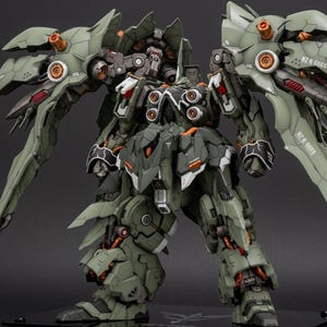 May include: A detailed, olive green and gray model of a mechanical robot with large wings. The model has intricate details, including orange accents and various mechanical components. The robot is posed in a dynamic stance, showcasing its design.