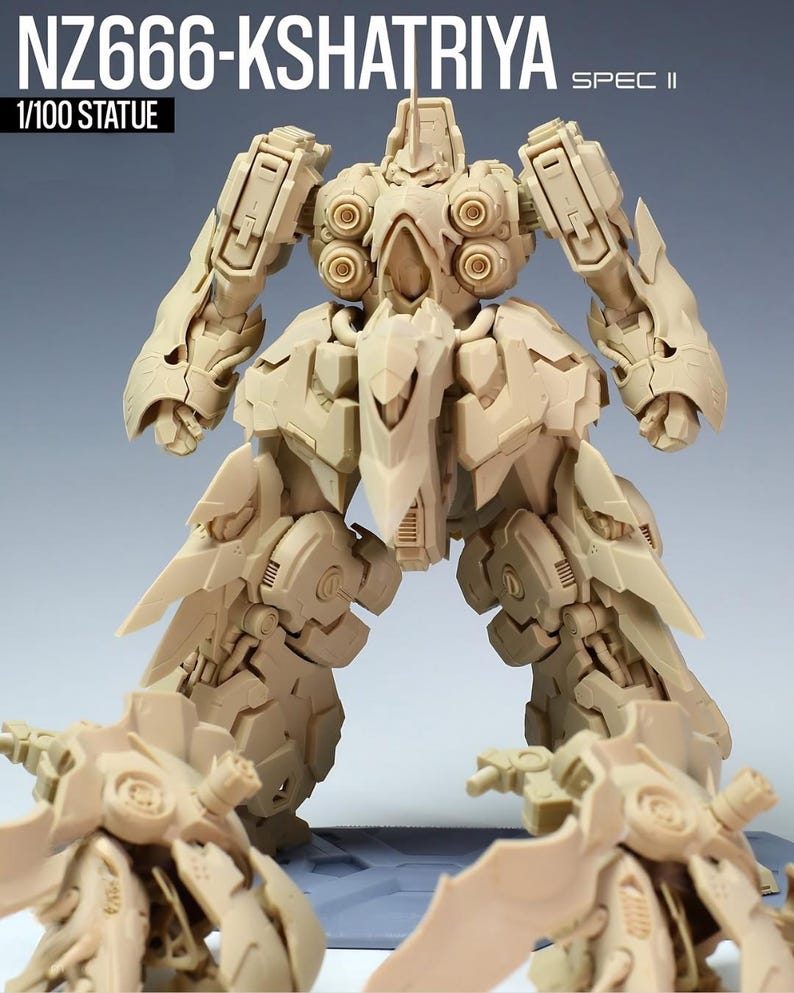 May include: A beige 1/100 scale statue of a robot, labeled "NZ666-KSHATRIYA SPEC II." The robot has detailed mechanical features, including articulated limbs, circular shoulder components, and sharp, wing-like structures extending from the legs.